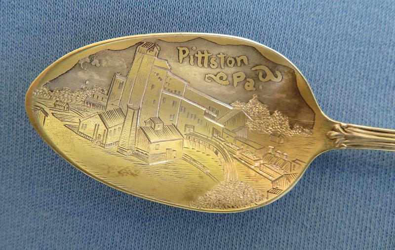Souvenir Mining Spoon Bowl Pittston PA.JPG - SOUVENIR MINING SPOON PITTSTON PA - Sterling silver spoon, 4 3/4 in. long, engraved colliery mining scene in gold-washed bowl with marking PITTSTON PA., ca.1900, reverse with Sterling marking, maker’s mark and PAT 1892  [Pittston is a city located within Pennsylvania's Coal Region in Luzerne County. Situated between Scranton and Wilkes-Barre, the city gained prominence in the late 19th and early 20th centuries as an active anthracite coal mining city, drawing a large portion of its labor force from European immigrants. The population was 7,739 as of the 2010 census, making it the fourth largest city in Luzerne County. At its peak in 1920, the population of Pittston was 18,497.  The first discovery of anthracite coal in the Wyoming Valley occurred around 1770. The first mine was established in 1775 near Pittston. With the opening of a canal in the 1830s, Pittston became an important link in the coal industry. The anthracite and railroad industry attracted thousands of immigrants, making Pittston a true melting pot with once-distinct ethnic and class neighborhoods. The population of Pittston boomed in the late 19th century. The boom continued well into the 20th century. The anthracite coal mining industry, and its extensive use of child labor in the early part of the 20th century, was one of the industries targeted by the National Child Labor Committee and its hired photographer, Lewis Hine. Many of Hine's subjects were photographed in the mines and coal fields in and around Pittston between 1908 and 1912. The impact of the Hine photographs led to the enactment of child labor laws across the country.  Anthracite coal mining remained a major industry in the Pittston region until the Knox Mine Disaster. It essentially killed the industry in Northeastern Pennsylvania. On January 22, 1959, the ice-laden Susquehanna River broke through the roof of the River Slope Mine of the Knox Coal Company in nearby Port Griffith. This allowed for billions of gallons of river water to flood the interconnected mines. It took three days to plug the hole in the riverbed, which was done by dumping large railroad cars, smaller mine cars, culm, and other debris into the whirlpool formed by the water draining into the mine.  Sixty-nine miners escaped; twelve miners died and their bodies were never recovered.]